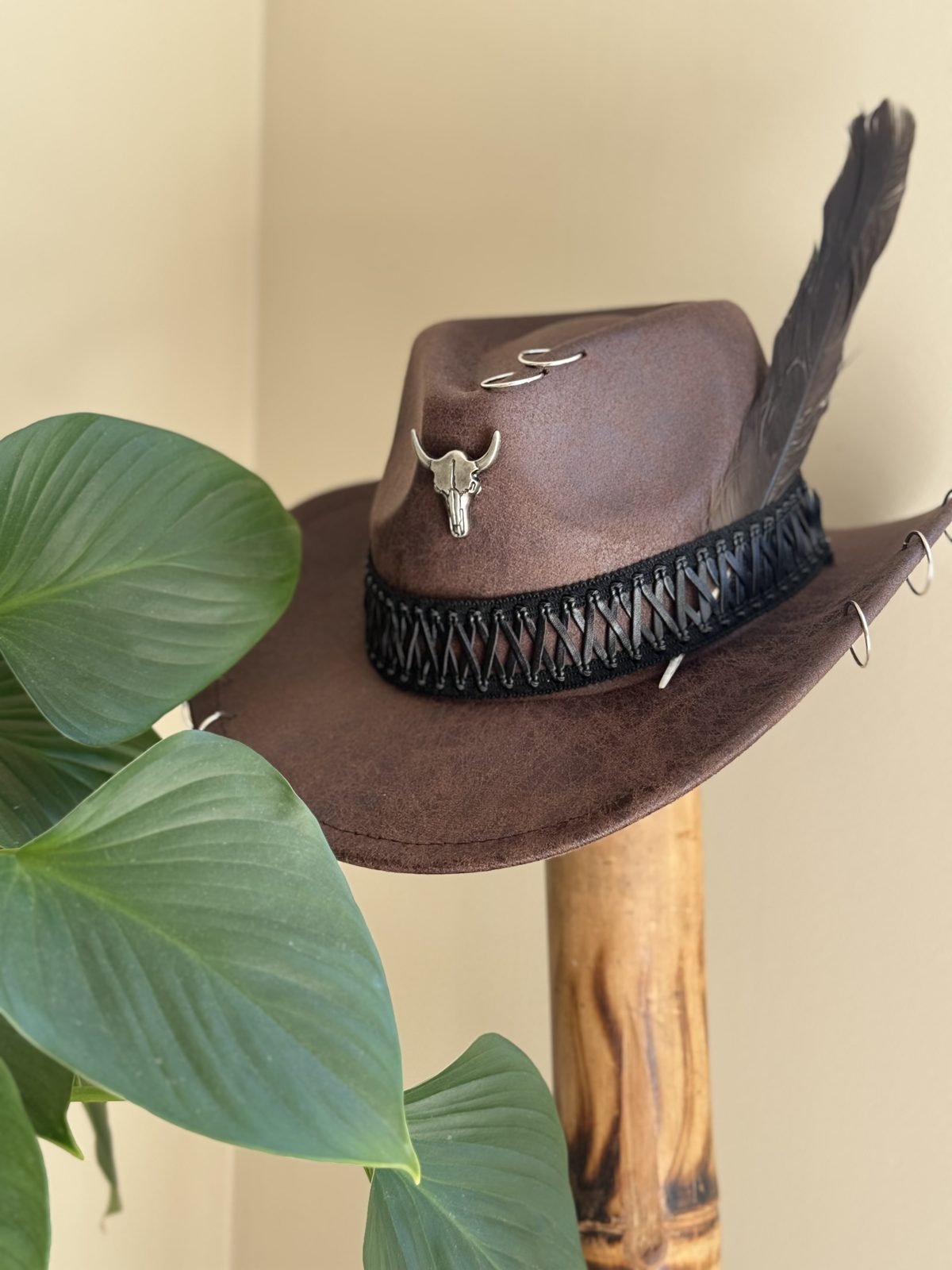 Brown wide-brim hat with bull-skull charm and raven feather