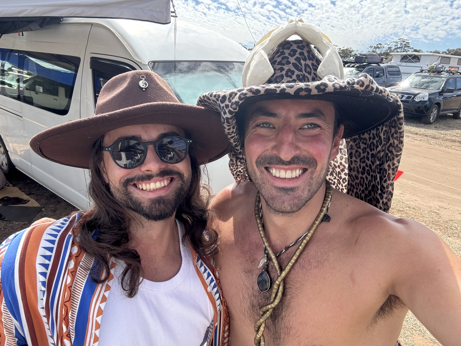 Two friends smiling wearing fedoras at a festival