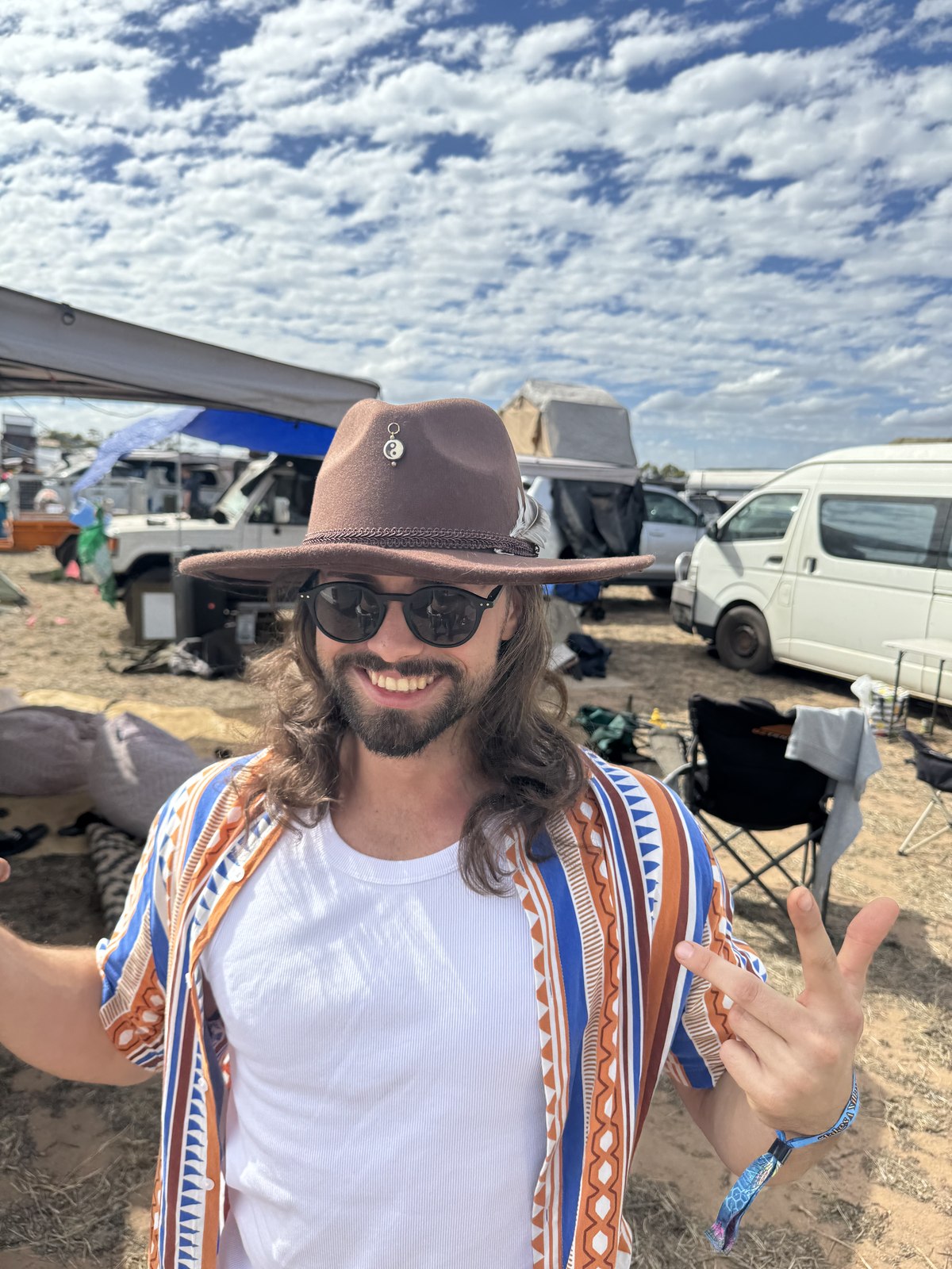 Man giving a peace sign wearing a brown fedora at a festival