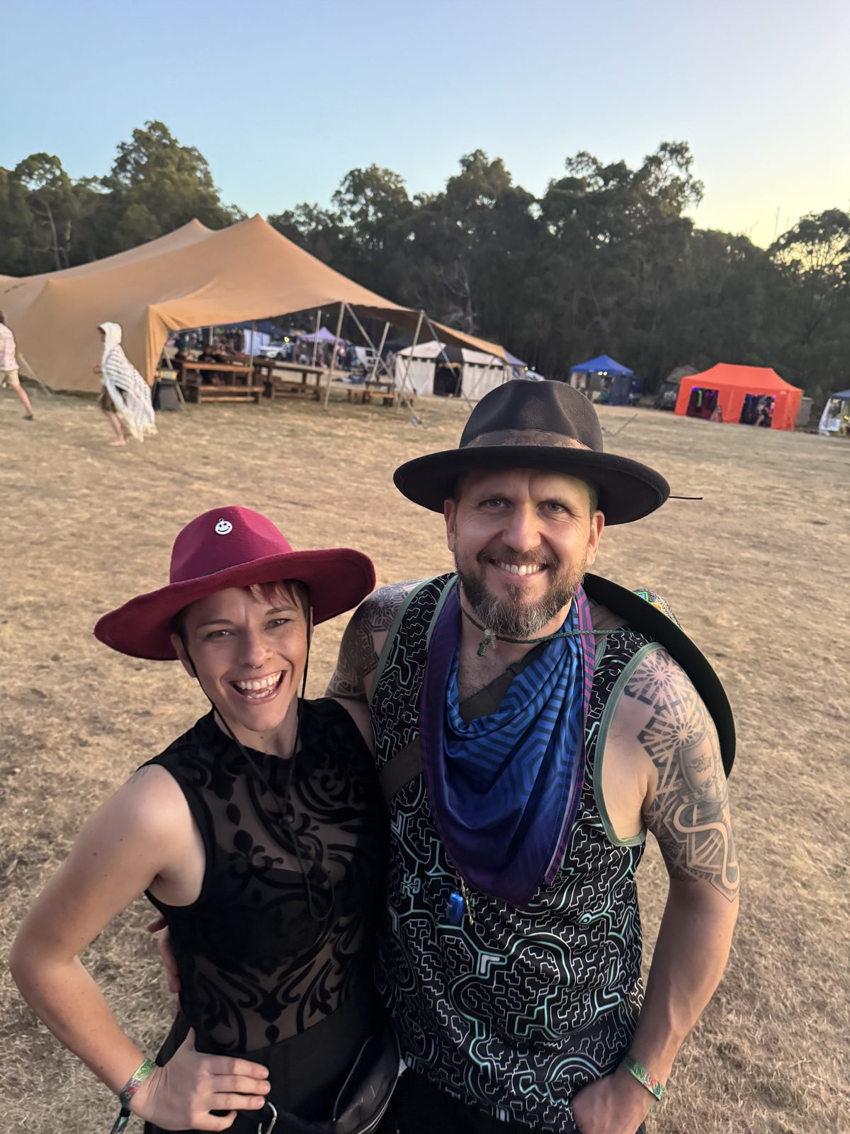 Two people smiling wearing fedoras at a festival