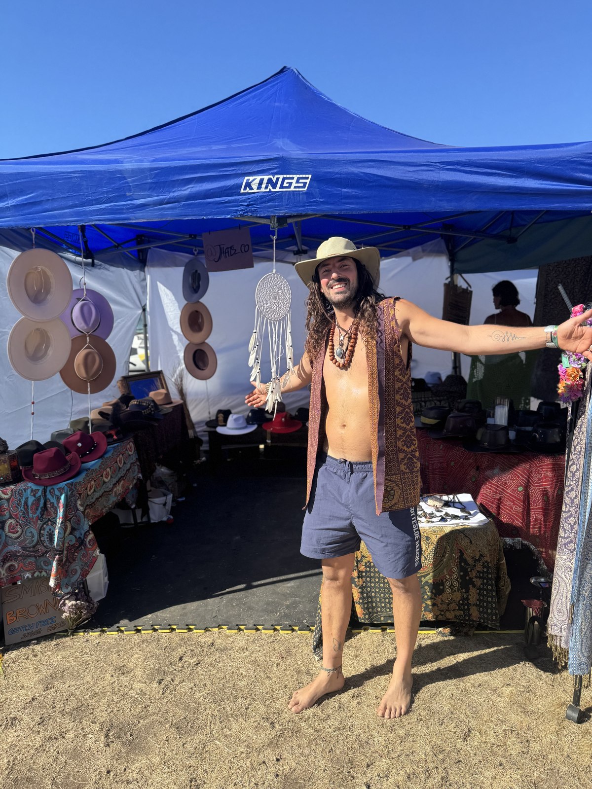 Man at a market stall surrounded by hanging fedoras